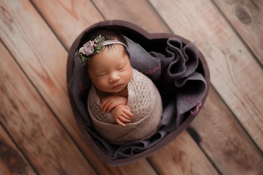 Niedliches Neugeborenen Baby in einem Herz Korb und lila Accessoires bei neugeborenen Babyfotoshooting mit Fotografin aus Munchen